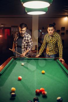 Two male billiard players with cue at the table with colorful balls, poolroom. Men plays american pool game in sport bar