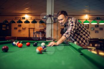 Male billiard player with cue at the table with colorful balls. Man plays american pool game in sport bar
