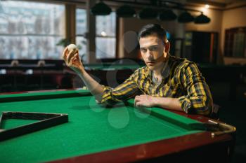 Male billiard player holds white ball at the green table. Man plays american pool game in sport bar