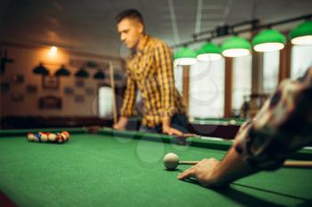 Two male billiard players with cue at the table with colorful balls. Men plays american pool in sport bar