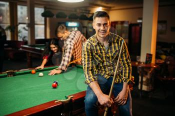 Two male billiard players with cues poses at the table with colorful balls, poolroom. Men plays american pool game in the sport bar