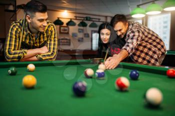 Billiard players with cues at the table with colorful balls, friends in poolroom. Group plays american pool game in sport bar