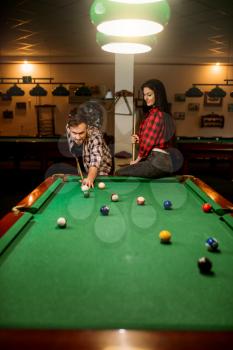 Family couple plays in billiard room. Man and woman leisures, american pool game, male player aiming to shot
