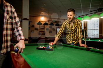 Two male billiard players places colorful balls, poolroom. Men plays american pool game in sport club