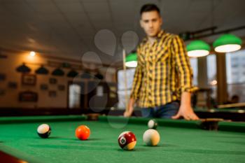 Male billiard player with cue, view from the table with colorful balls, poolroom interior on background. Man plays american pool game in sport bar