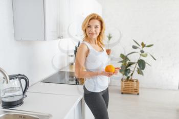 Sporty woman throws up an orange, fit breakfast on the kitchen. Female person at home in the morning, lifestyle