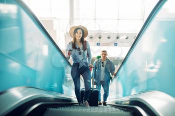 Couple with luggage climb the escalator in airport. Passengers with baggage in air terminal, happy family journey, summer travel