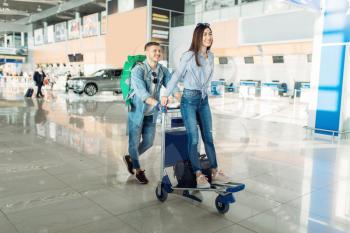 Male tourist roll the cart with luggage and his wife in airport. Passengers with baggage in air terminal, happy journey, summer travel