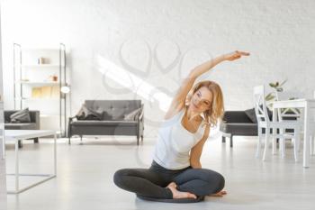 Yuong woman sitting on the floor in yoga pose, living room interior in white tones on background