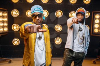 Two black rappers in caps, artists poses on stage with spotlights on background. Rap performers on scene with lights, underground music, urban style