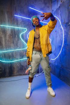 Black rapper in underpass neon light on background. Rap performer in club with grunge walls, underground music concert, urban style