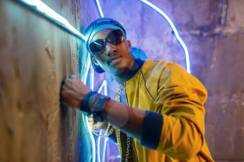 Black rapper in underpass neon light on background. Rap performer in club with grunge walls, underground music