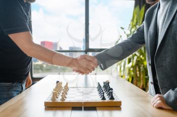 Male chess players shake hands before the game. Two chessplayers begin the intellectual tournament indoors. Chessboard on the table
