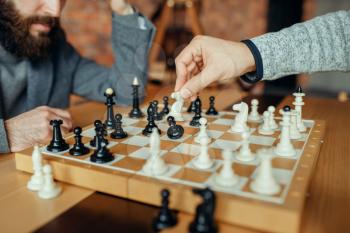 Male chess players playing at board, white knight takes pawn. Two chessplayers begin the intellectual tournament indoors. Chessboard on wooden table
