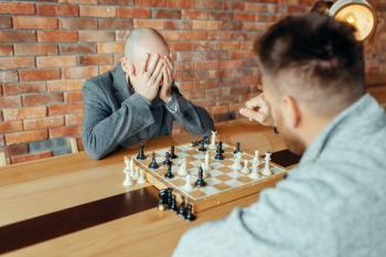 Male chess players playing at board, white wins, mate. Two chessplayers begin the intellectual tournament indoors. Chessboard on wooden table