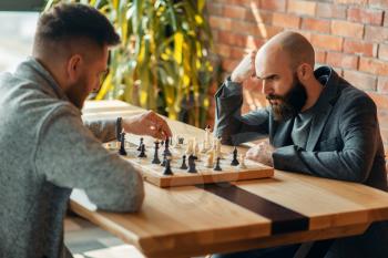 Male chess players playing at board, move the black elephant. Two chessplayers begin the intellectual tournament indoors. Chessboard on wooden table