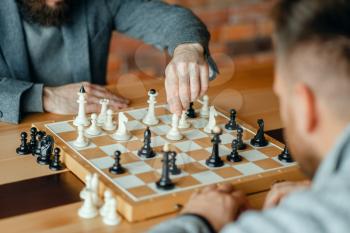 Male chess players playing, thinking process. Two chessplayers begin the intellectual tournament indoors. Chessboard on wooden table, strategy game