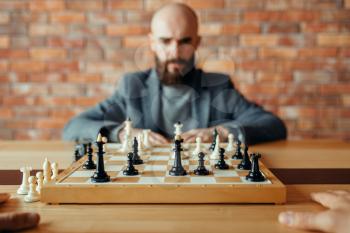 Male chess player, thinking process. Two chessplayers begin the intellectual tournament indoors. Chessboard on wooden table, strategy game