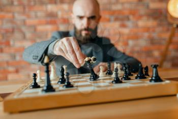 Male chess player playing, white figure move, the loss of the black queen. Chessplayer at board, front view, intellectual tournament indoors. Chessboard on wooden table, strategy game