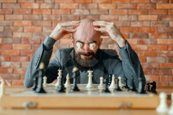 Male chess player with figures in the eyes, thinking process. Chessplayer at board, intellectual tournament indoors. Chessboard on wooden table, strategy game