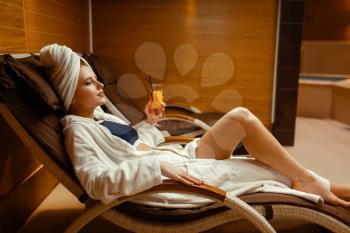 Sexy girl in bathrobe and towel on the head relaxing with cocktail in spa chair. Relaxation leisure, healthy lifestyle, attractive woman resting in armchair, beauty salon
