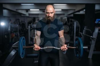 Muscular athlete in sportswear takes weight, training in gym. Bearded man on workout in sport club