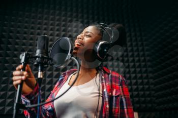 Female performer in headphones songs in audio recording studio. Musician  listens composition, professional music mixing
