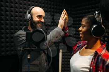 Male and female performers in headphones songs in audio recording studio. Musicians on record, professional music mixing