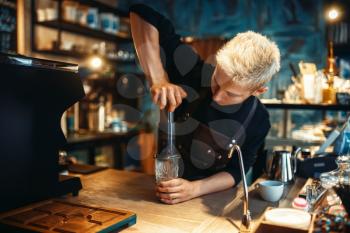 Young male barista makes fresh espresso, black coffee preparation at cafe counter. Barman works in cafeteria, bartender occupation