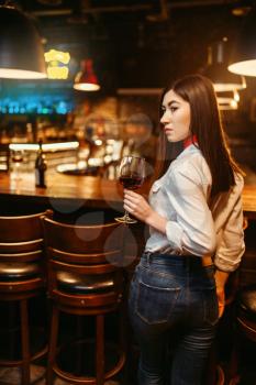 Young attractive woman with glass of red wine at wooden bar counter. Female customer leisures in pub