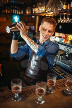 Male bartender in apron works with shaker at the bar counter. Alcohol beverage preparation. Barman occupation
