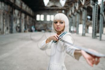 Pretty anime style blonde woman with sword. Cosplay fashion, japanese culture, doll with blade on abandoned factory, cute girl with makeup