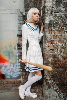 Anime girl with baseball bat. Cosplay fashion, asian culture, doll in uniform, cute woman with makeup in abandoned factory shop