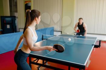 Man and woman playing ping pong indoors. Couple in sportswear holds rackets and plays table tennis in gym