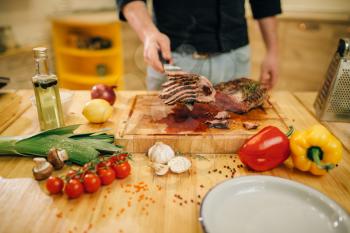 Male chef hands with knife cuts roasted meat on slices, top view. Man preparing beef with vegetables