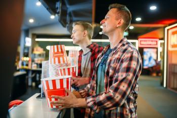 Two male friends buying popcorn in cinema bar before the showtime. Youth in movie theater hall, entertainment lifestyle