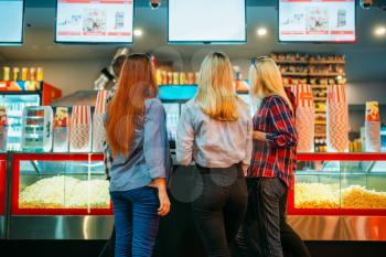 Friends choosing food in cinema bar before the screening, back view. Male and female youth in movie theater
