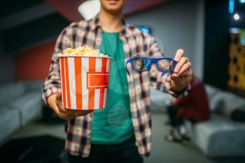 Male spectator with 3d glasses and popcorn in cinema hall before the showtime. Man in movie theater, entertainment lifestyle