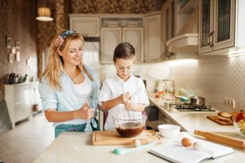Young mother with her son mixing melted chocolate in a bowl. Cute woman and little boy cooking on the kitchen. Happy family prepares sweet dessert at the counter