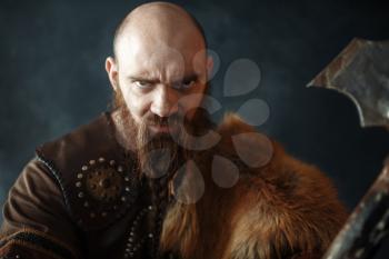 Portrait of viking with axe, martial spirit, barbarian image. Ancient warrior in smoke on dark background