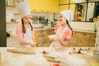 Two little girls chefs roll out the dough with rolling pins, cookies preparation on the kitchen. Kids cooking pastry and having fun, children cooks preparing cake