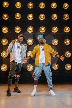 Two black rappers in caps poses on stage with spotlights on background. Rap performers on scene with lights, underground music, urban style