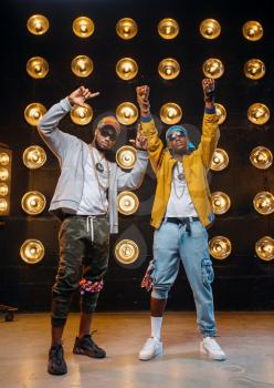 Two black rappers in caps, perfomance on stage with spotlights on background. Rap performers on scene with lights, underground music concert, urban style