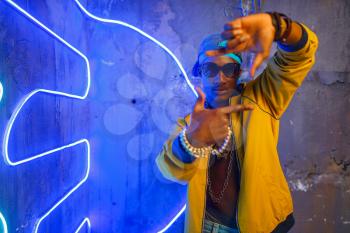 Black rapper in underpass neon light on background. Rap performer in club with grunge walls, underground music concert