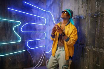 Black rapper in underpass neon lights on background. Rap performer in club with grunge walls, underground