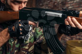 Cruel terrorist in uniform aiming from a kalashnikov rifle closeup, man with weapon. Terrorism and terror concept