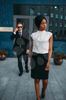 Black business woman bodyguard in suit and sunglasses on background. Security guard is a risky profession, protection of VIPs, guarding occupation, private safety
