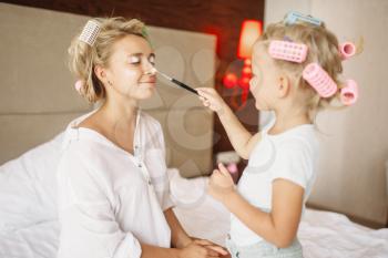 Daughter makes a funny makeup to her mother in bedroom at home. Parent feeling, togetherness, happy times