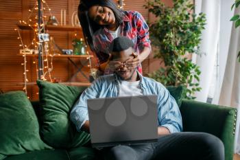 Black couple with laptop having fun on sofa at home. Happy african love couple leisures in their house, cheerful family relaxing in living room