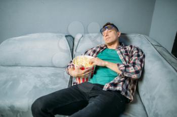 Male spectator with popcorn sleeping on sofa in cinema hall before the showtime. Man in movie theater, entertainment lifestyle
